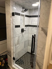 a shower with a glass door and black and white tile