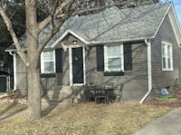 a small gray house with a tree in front of it